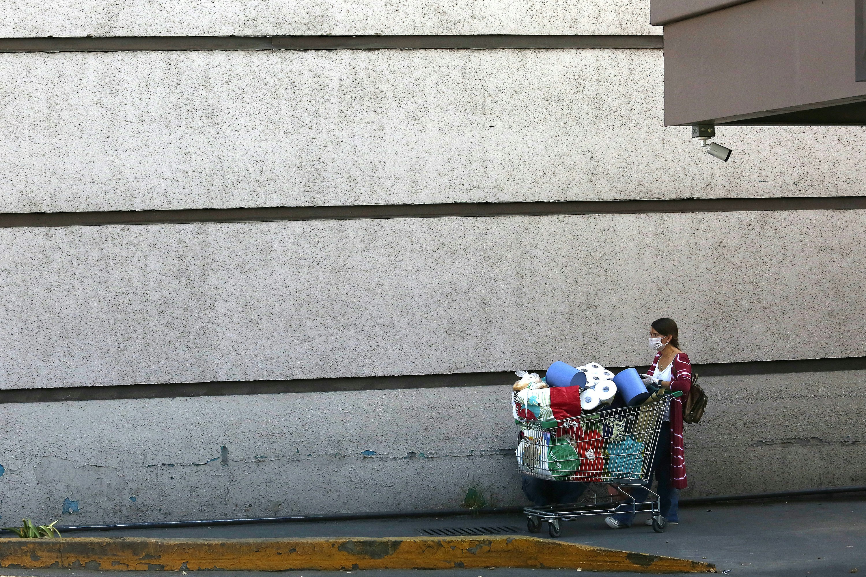 A masked woman walks with a shopping cart piled high with supplies